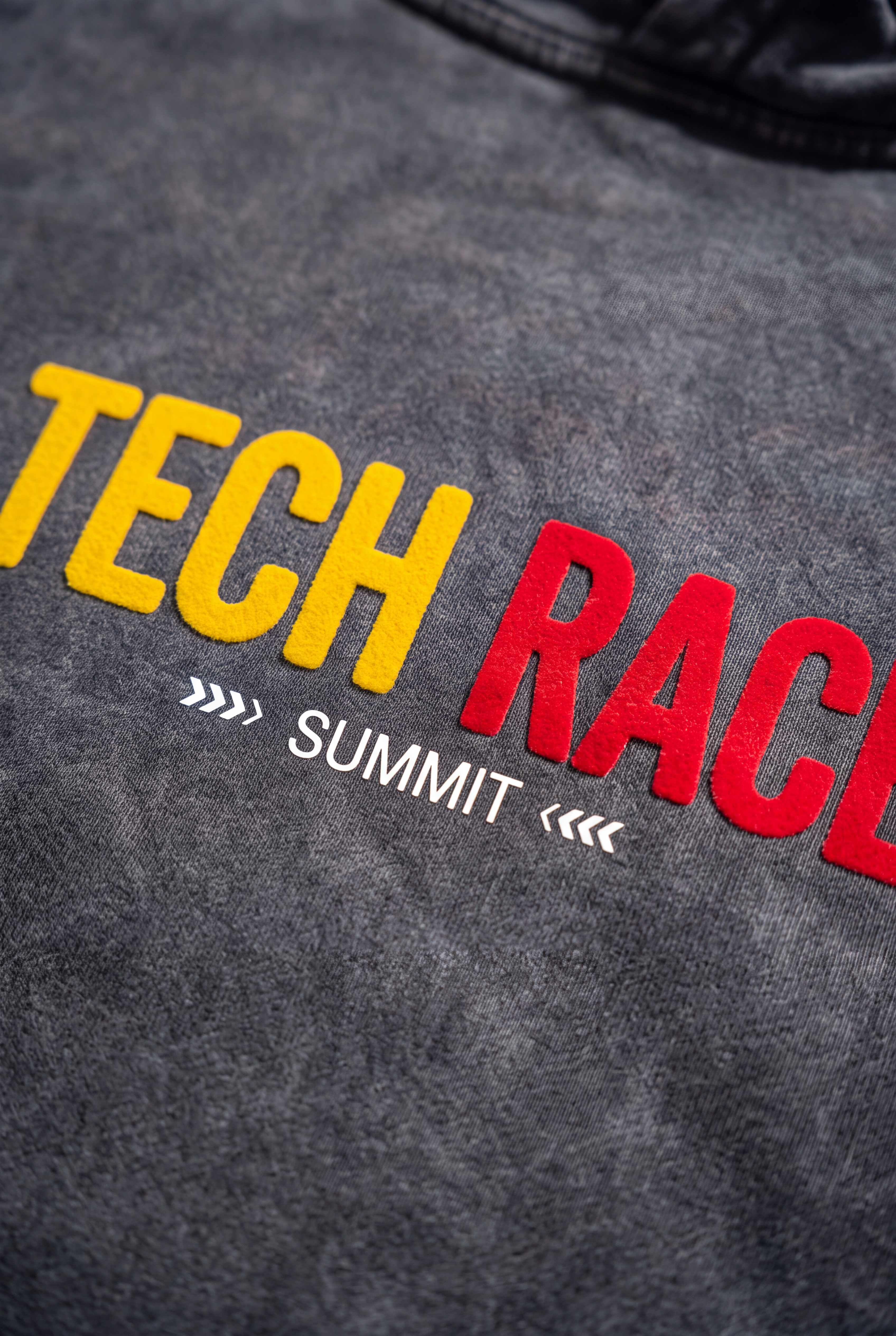Close-up of textured yellow and red Tech Race lettering on the grey hoodie